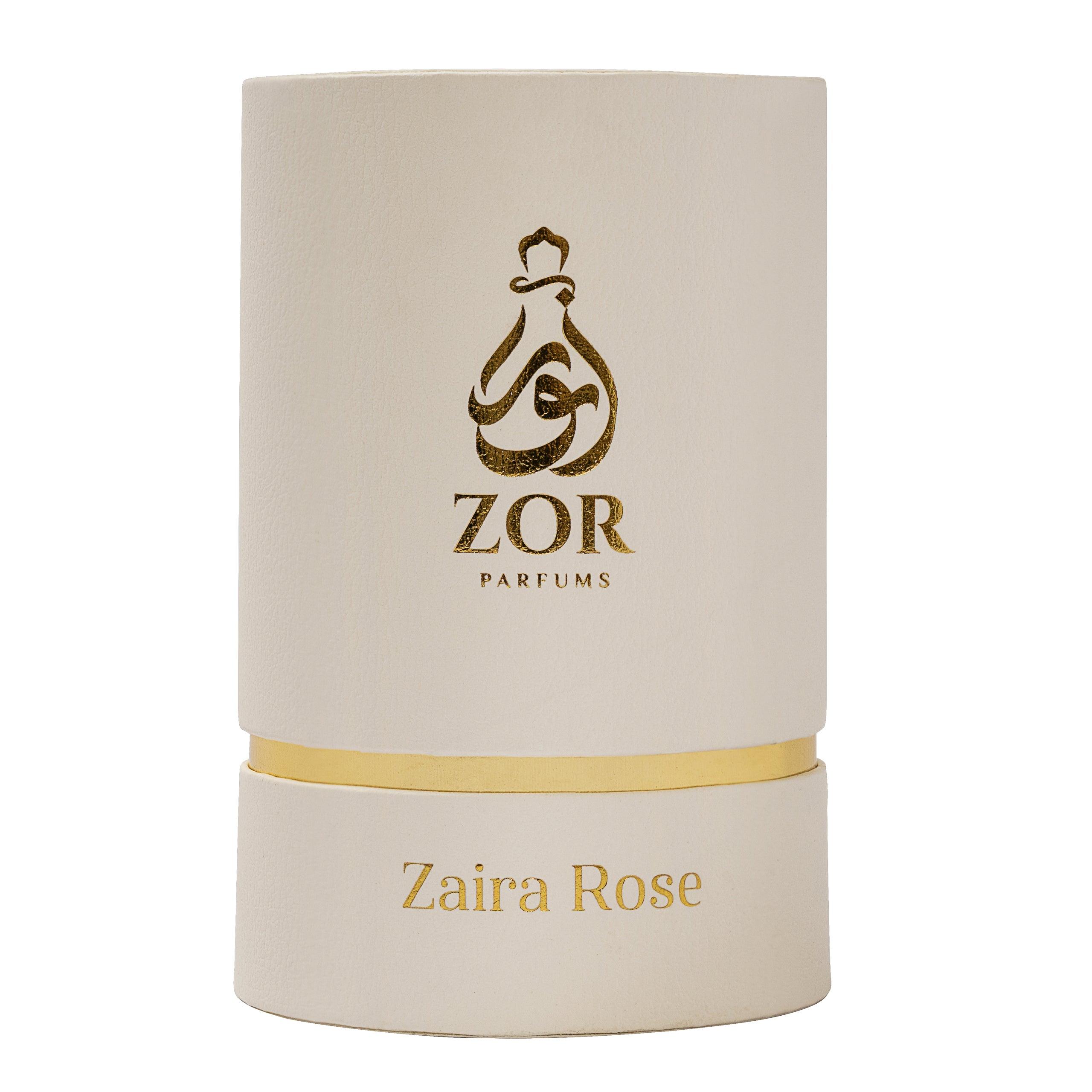 A cylindrical white box with gold accents, labeled "ZOR Parfums" featuring a stylized perfume bottle logo. Below, the name "Zaira Rose" is printed in gold letters, hinting at a luxurious fragrance infused with notes of honey and oud.